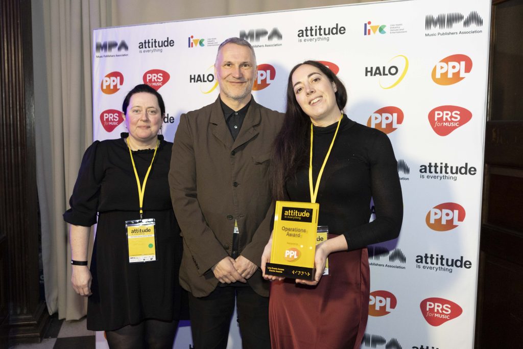 Hayley Woodbridge from Victorious Festival, Jez Bell from PPL, and Katherine Sim from Victorious Festival stand in front of the step-and-repeat wall which shows logos for Attitude is Everything, and the event’s sponsors: Halo, PPL, LIVE, and the MPA. Katherine holds the Operations Award, awarded to Victorious.